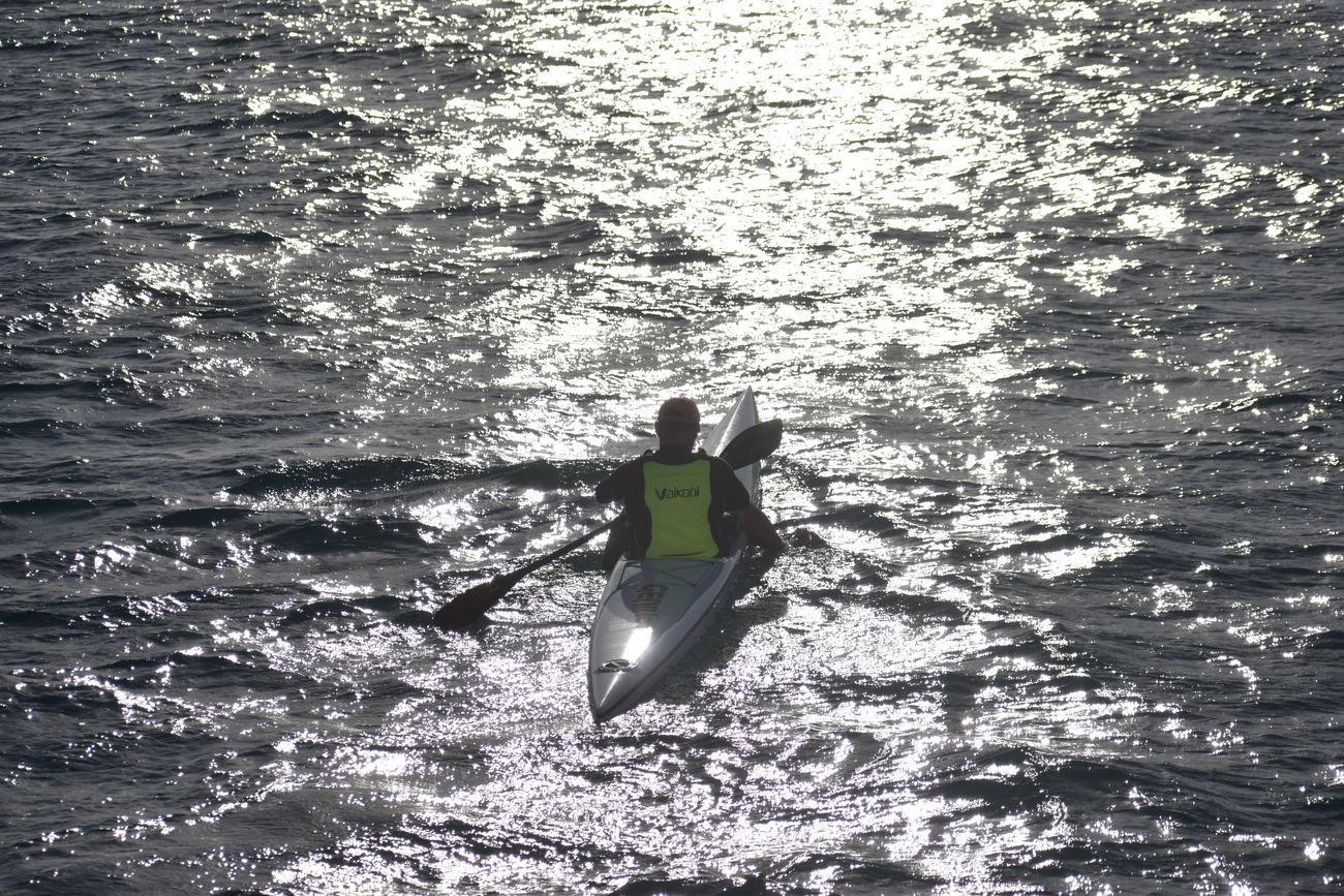 A paddler on a surf ski heading into sun-glittered water