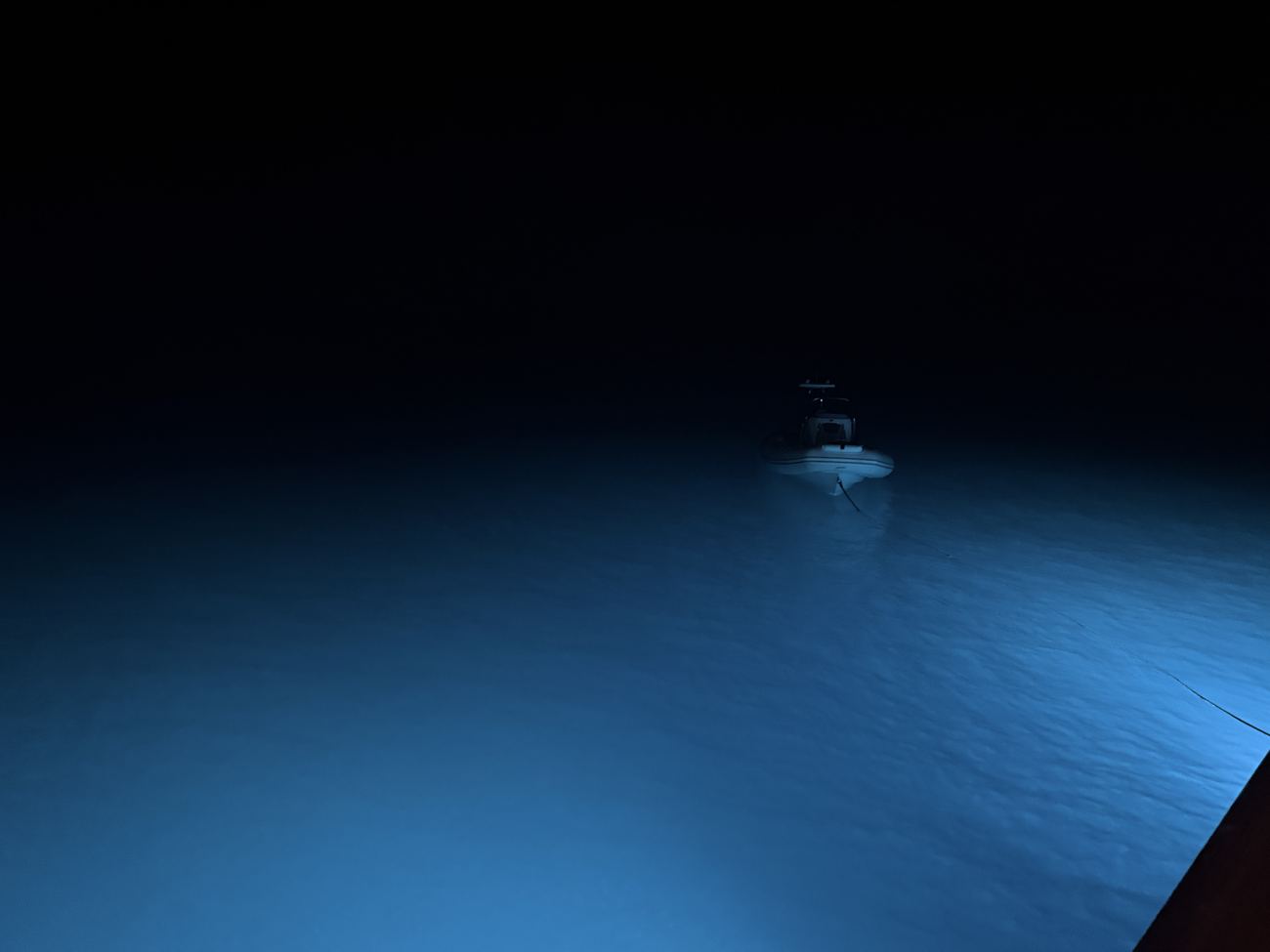 The stern lights glowing blue in the dark water at anchor