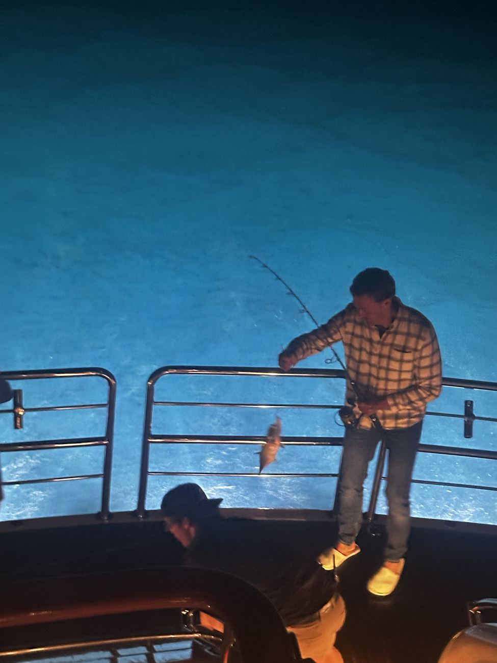 Sean lifting a fish from the electric blue water at the stern
