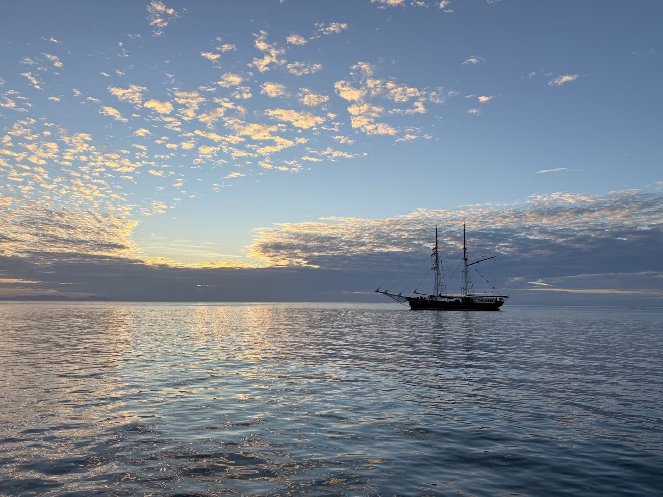 A tall ship at anchor, silhouetted against the dusk sky