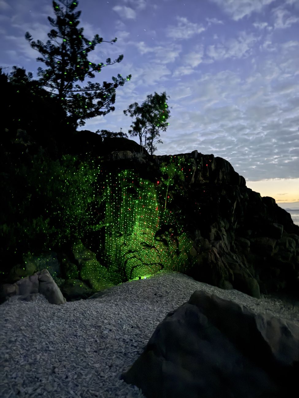 Green laser light scattered across the cliff above the coral beach at dusk