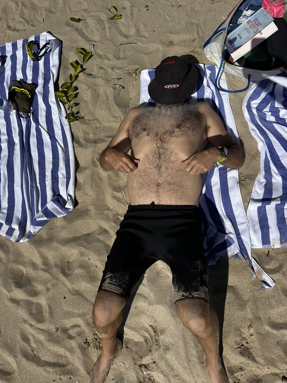 A guest starfished on the beach, hat over face
